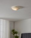Runde Deckenleuchte mit Milchglas in modernem Schlafzimmer, weiße Wände, Zimmerpflanze und Tageslicht.