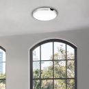 Moderne LED-Deckenleuchte rund, weiß, im hellen Raum mit großen Fenstern und Blick ins Grüne.