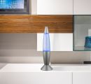 Silberne Lavalampe mit blauem Licht auf weißem Regal vor moderner Holzwand im Wohnzimmer.