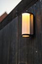 Moderne LED-Außenwandleuchte leuchtet an einer dunklen Holzfassade bei Dämmerung, energiesparende Beleuchtung.