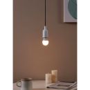 Moderne Hängelampe leuchtet über Tisch mit Tasse, Kerzen und Zeitung vor beiger Wand, gemütliche Atmosphäre.