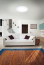 Modernes Wohnzimmer mit weißem Sofa, buntem Teppich, Treppe und minimalistischer Einrichtung in hellem Raum.