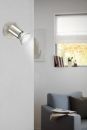 Moderne LED-Wandleuchte aus Edelstahl leuchtet in hellem Wohnzimmer mit Sofa, Fenster und Bücherregal.