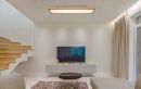 Modernes Wohnzimmer mit Flachbildfernseher, Holztreppe, Teppich und minimalistischer Einrichtung.