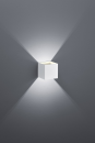 Moderne LED-Wandleuchte in Würfelform, weiß, an grauer Wand, strahlt Licht nach oben und unten ab.
